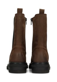 Botas de tobillo de cuero marrón con una textura suave, paneles laterales elásticos y una suela de plataforma negra gruesa. Presentan una lengüeta trasera y cierre de cremallera.