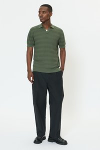 Zelené polo s krátkými rukávy a výstřihem do V, s strukturovanou tkaninou, doplněné černými volnými kalhotami a černými šněrovacími botami.