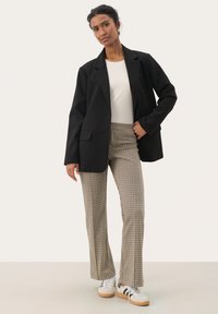 Zwarte oversized blazer, witte top, geruite flared broek, witte sneakers met zwarte strepen. Gladde texturen en een getailleerde pasvorm.