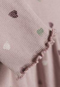 Rosa ribbet stoff med små hjerte mønstre i grønn, hvit og mørk lilla, med en volangdetalj på ermene.