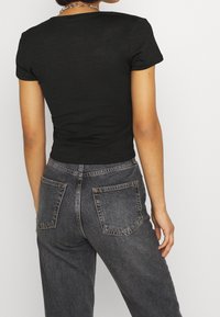 Svart ribbad kortärmad topp kombinerad med mörkgrå högmidjade jeans. Toppen har en figurnära design med rundad halsringning och mjuk textur.