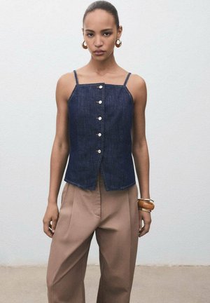 Top in denim senza maniche con scollatura quadrata, bottoni frontali e una leggera forma a A. Abbinato a pantaloni beige a vita alta.