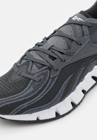 Chaussure de sport grise avec tige en maille texturée, superpositions synthétiques et lacets ton sur ton. Dotée d'une semelle extérieure blanche en moulé pour un confort accru.