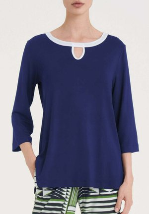 Donna che indossa una maglia blu navy a maniche lunghe con scollo a goccia bianco, abbinata a pantaloni a righe verdi, nere e bianche.