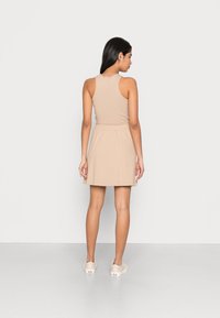 Vestido bege sem mangas com um corpete ajustado e saia rodada, feito de um tecido leve. Combinado com sapatos brancos de slip-on.