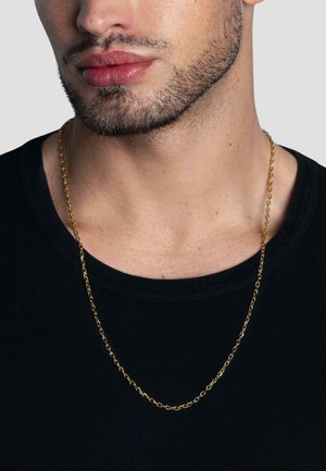 Guld metal kæde halskæde ligger på en bar hals og har fine led og en glat, blank finish. Personen har en sort crew-neck skjorte på.