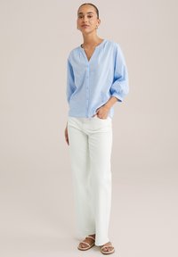 Light blue, long-sleeve button-up shirt with a V-neck and embroidered details, paired with white wide-leg pants and sandals.