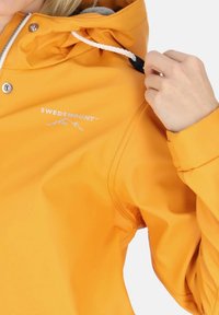 Yellow waterproof jacket featuring a hood, drawstring, silver snaps, and a white logo on the front, with smooth, shiny texture.