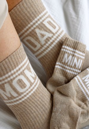 Chaussettes beiges assorties pour adulte et enfant, étiquetées « MOM » et « MINI » en lettres blanches avec des accents rayés.