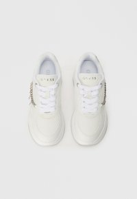 Bijele tenisice s mrežastim i sintetičkim gornjištem, ravnim bijelim vezicama i srebrnim detaljima. Ime branda "GUESS" na jeziku.