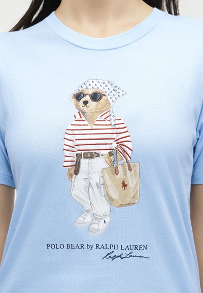 Εικονογράφηση αρκούδας που φοράει γυαλιά ηλίου, ριγέ πουκάμισο, λευκό παντελόνι, αθλητικά παπούτσια και μπαντάνα, κρατώντας μια τσάντα ώμου σε ένα ανοιχτό μπλε πουκάμισο.