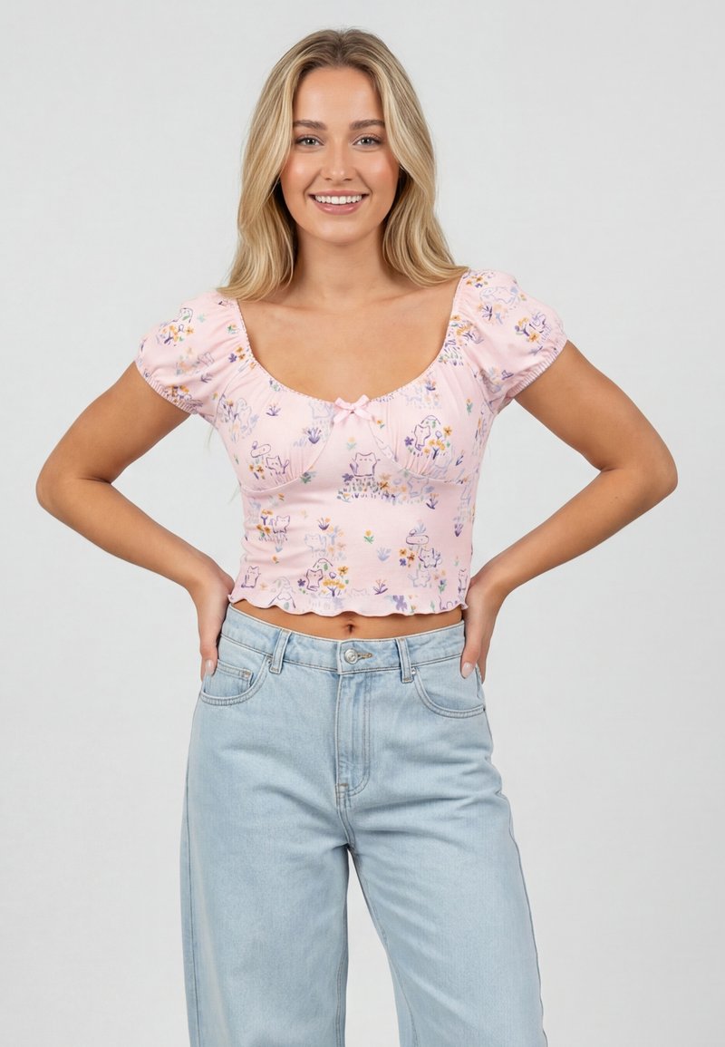Jeune femme souriante, portant un top court à fleurs rose clair avec des manches courtes bouffantes et un jean taille haute bleu clair, mains sur les hanches.