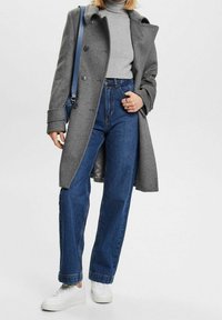 Manteau en laine gris avec col cranté, pull à col roulé gris, jean bleu taille haute et baskets blanches. Comprend un sac à bandoulière bleu.
