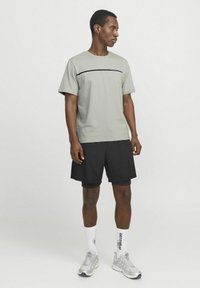 Lys grå t-shirt med en vandret sort linje, parret med sorte shorts. Tekstureret stof, korte ærmer og atletisk pasform. Sølvfarvede løbesko.