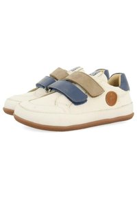 Zapatillas de cuero blanco con correas de Velcro azul y beige, una parte superior texturizada y suelas de goma marrón. Presenta un logo circular en el costado.