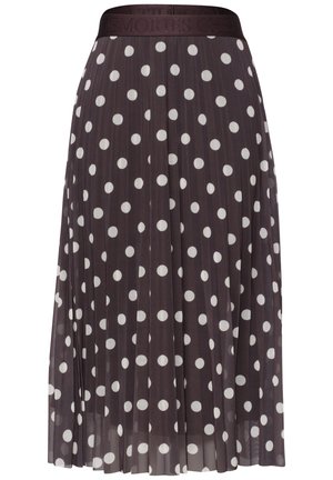 Henkilön vyötärö ja kädet, joka pukeutunut mustaan plissoonihameeseen, jossa on valkoisia pilkkuja, ja siihen sopivaan mustaan yläosaan.