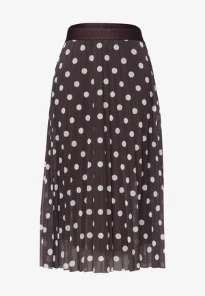 Henkilön vyötärö ja kädet, joka pukeutunut mustaan plissoonihameeseen, jossa on valkoisia pilkkuja, ja siihen sopivaan mustaan yläosaan.