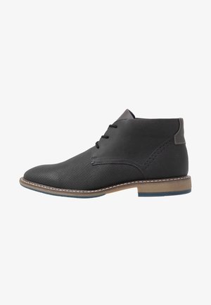 Bottines en cuir noir avec un design perforé, bout rond, coutures discrètes et semelle beige. Fermeture à lacets et un accent kaki.
