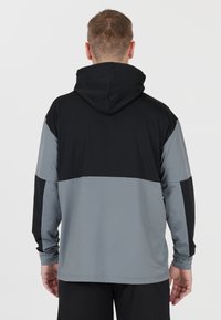 Huvtröja med svart övre del och grå nederdel. Tillverkad av ett slätt tyg med långa ärmar och en avslappnad passform.