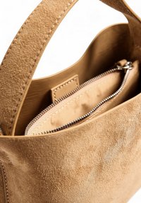 Borsa in suede beige con una texture liscia, dotata di una tasca interna con zip e di un manico cucito. Design pulito e minimalista.