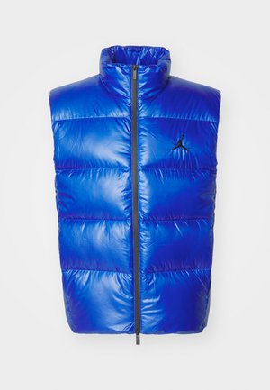 Blue puffer vest with high collar, vertical quilted design, front zipper, featuring a black Jordan logo on the left chest.