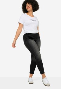 Jeggings negros de cintura alta, con un acabado sutilmente desgastado, combinados con una camiseta blanca que presenta la palabra "Jeggings". Zapatillas blancas.