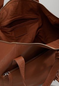 Bolso de mano de cuero marrón con una abertura con cremallera, interior de textura suave y un bolsillo lateral con un forro de tela suave.