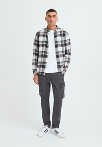 Rutet flanellskjorte i svart og hvitt over en hvit t-skjorte, kombinert med grå cargobukser med sidelommer og svarte detaljer. Hvite sneakers.