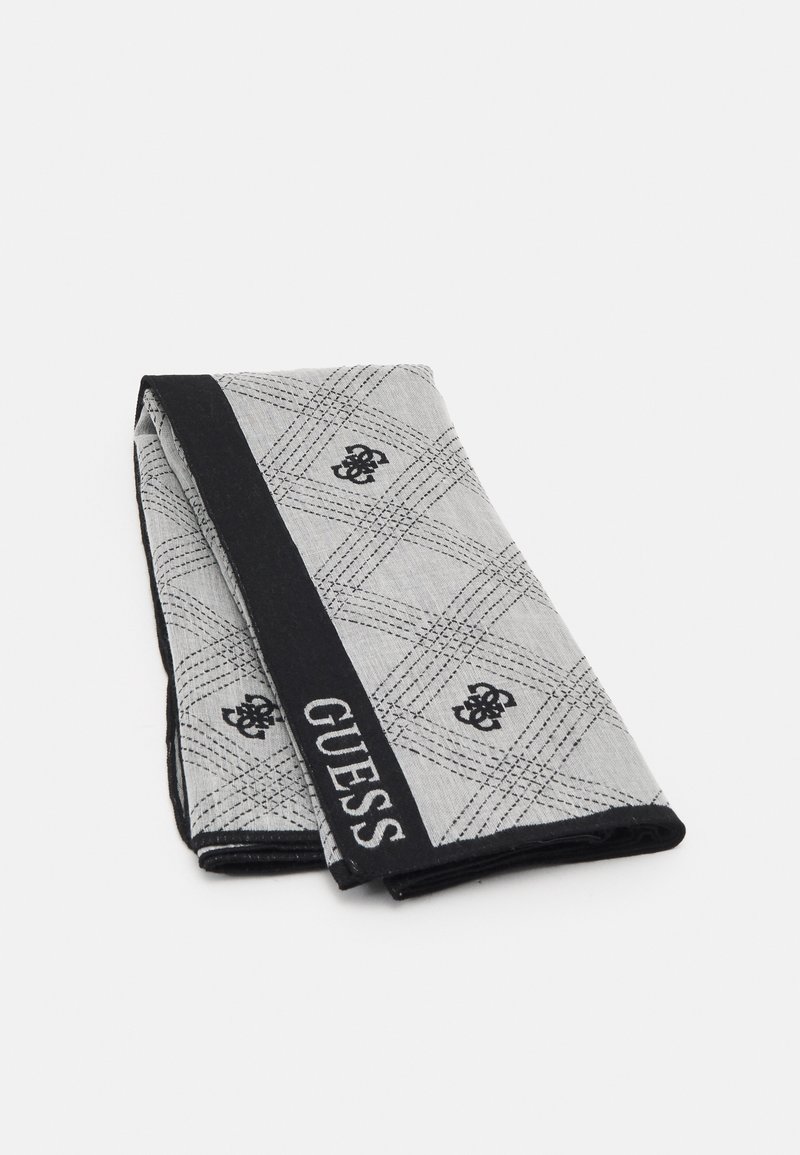 Tissu gris plié avec grille diagonale noire et motifs floraux, bande de bordure noire avec "GUESS" en lettres blanches.