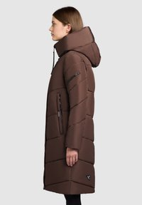 Bruine geïsoleerde pufferjack met een hoge kraag en grote capuchon, met een diagonaal quiltpatroon en ritszakken aan de zijkant.