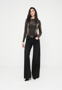 Μεταλλικό μπρονζέ μπλουζάκι με μακριά μανίκια συνδυασμένο με μαύρα τζιν παντελόνια φαρδιάς γραμμής, με μαύρη ζώνη με ασημένια αγκράφα και μυτερές μαύρες γόβες.