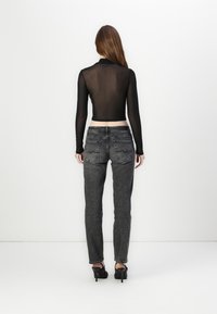 Zwarte doorschijnende top met lange mouwen en een cropped ontwerp, gecombineerd met grijze denim jeans met achterzakken en rafelige hems. Zwarte hakken maken de outfit compleet.