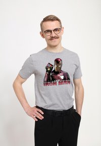 Camiseta de algodón gris con un gráfico de Iron Man y el texto "SOY IRON MAN" en rojo vivo. Mangas cortas; combinada con pantalones negros.