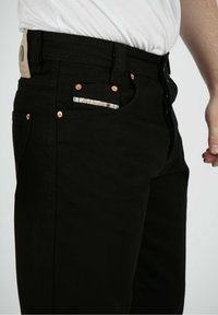 Svarta denimjeans med en slim-fit design, som har kopparfärgade nitar, en läderlapp i midjan och ett mönstrat inre fickdetalj.