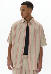 Camisa de boton corto de manga en tejido ligero, con rayas verticales en beige y coral, un bolsillo en el pecho y un corte relajado.