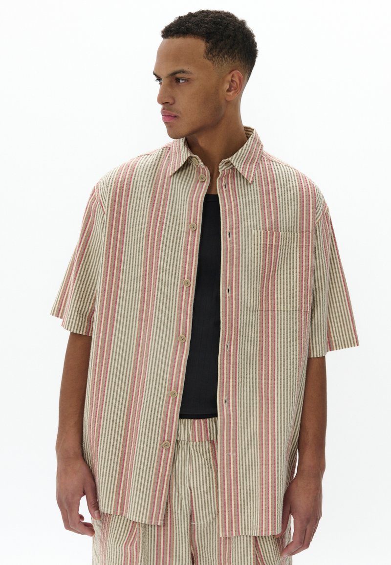 Camisa de boton corto de manga en tejido ligero, con rayas verticales en beige y coral, un bolsillo en el pecho y un corte relajado.