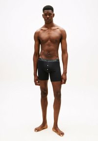 Boxer neri dal design aderente, con una vita marchiata che riporta la scritta "TOMMY HILFIGER." Il materiale sembra liscio ed elastico.