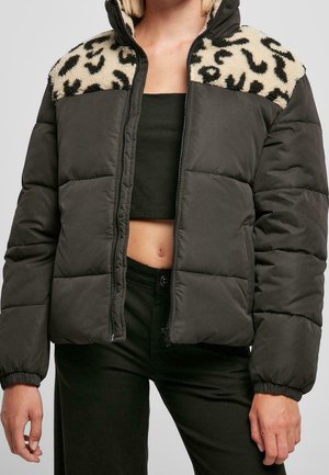 Woman wearing a black padded jacket with leopard print fleece on shoulders, unzipped over a black cropped top and black pants.