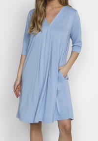 Světle modré šaty s výstřihem do V, tříčtvrtečními rukávy, bočními kapsami a volným střihem. Vyrobeny z měkké látky s hladkou strukturou.