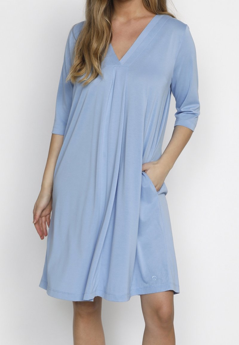 Světle modré šaty s výstřihem do V, tříčtvrtečními rukávy, bočními kapsami a volným střihem. Vyrobeny z měkké látky s hladkou strukturou.
