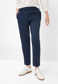 Marineblauwe, taps toelopende sweatpants met een elastische tailleband en zijzakken, gecombineerd met witte sneakers met zilveren accenten.