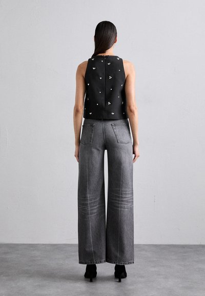 Črn kratki top z dekorativnimi srebrnimi detajli, v kombinaciji z širokimi sivo-denim hlačami z izrazitimi šivi in dvema zadnjima žepoma.