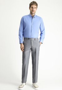 Camicia azzurro chiaro con bottoni, pantaloni grigi plissettati, sneakers bianche. La camicia ha un colletto strutturato; i pantaloni presentano una vestibilità su misura e una consistenza morbida.