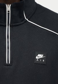 Μαύρο φούτερ με φερμουάρ στη λαιμόκοψη, λευκές λεπτομέρειες, απαλή υφή και τετράγωνο κονκάρδα με το λογότυπο Nike Air στο στήθος.