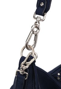 Zbliżenie na srebrne metalowe zapięcia i pierścienie łączące granatowo-niebieski skórzany pasek z dziurkowaną torbą w tym samym odcieniu.