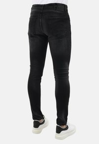 Zwarte denim skinny jeans met een middelhoog taille, voorzien van achterzakken en een gladde textuur, gecombineerd met witte en zwarte sneakers.