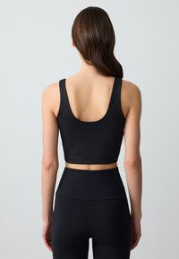 Czarny sportowy crop top z szerokimi ramiączkami, wycięciem na plecach i gładkim, elastycznym materiałem. W komplecie ze dopasowanymi legginsami o wysokim stanie.