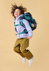 Dunkelblauer Rucksack mit weltraumthematischen Mustern, verstellbaren Trägern und einem runden Aufnäher. Lila Zip-Jacke, grüne Hose, weiße Turnschuhe.