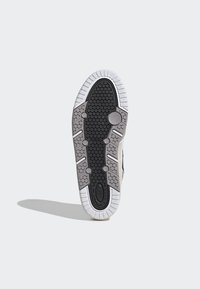 Podešev tenisky s černým gumovým povrchem, který obsahuje hexagonální vzory, bílý gumový okraj a kruhové prvky pro trakci.