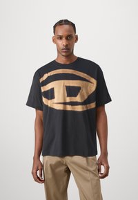 Sort bomulds T-shirt med et stort beige abstrakt design i midten. Korte ærmer og en afslappet pasform; glat overflade.